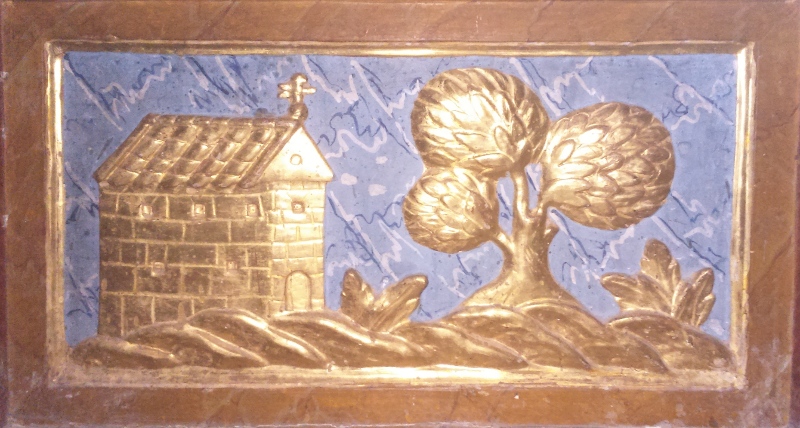 Paisaje esculpido en madera donde aparece una sencilla iglesia en el lado izquierdo y un árbol frondoso a su derecha