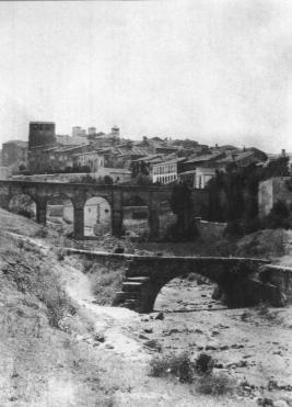 Fotografía antigua con puente en primer término y el acueducto de los Arcos al fondo