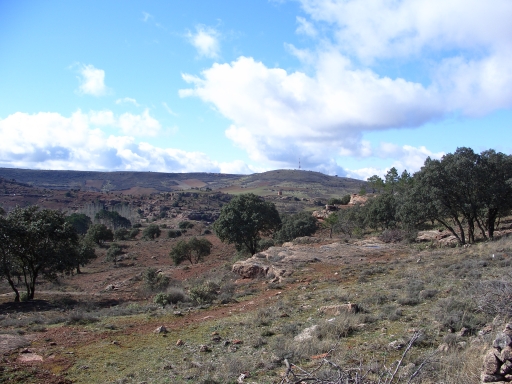 Paisaje con la zona minera, consistente en montes de areniscas rojizo-verdosas cubiertas por encinar. Al fondo se divisa el castillo