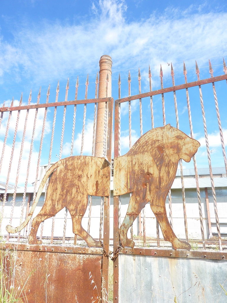 El león, símbolo de la fábrica, en la verja de la entrada principal a la misma. Tras él, la chimenea principal.