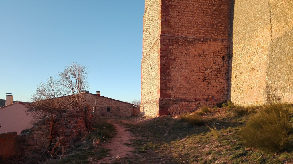 Camino flanqueado por un muro bajo a la izquierda y las murallas del castillo a la derecha, terminando en el muro trasero del Hostal de Doña Blanca