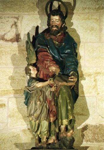 Escultura de madera policromada representando al apóstol San Mateo de pie, apoyándose para escribir su evangelio en la rodilla izquierda, que mantiene algo levantada. A su derecha un ángel le ofrece un tintero